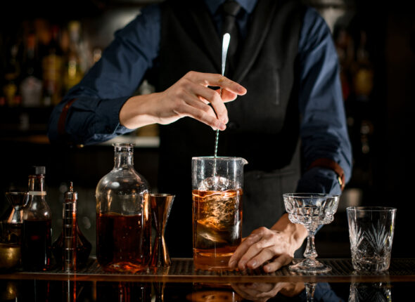 Professional,Bartender,Stirs,Cold,Cocktail,With,Spoon.,Several,Bottles,Of
